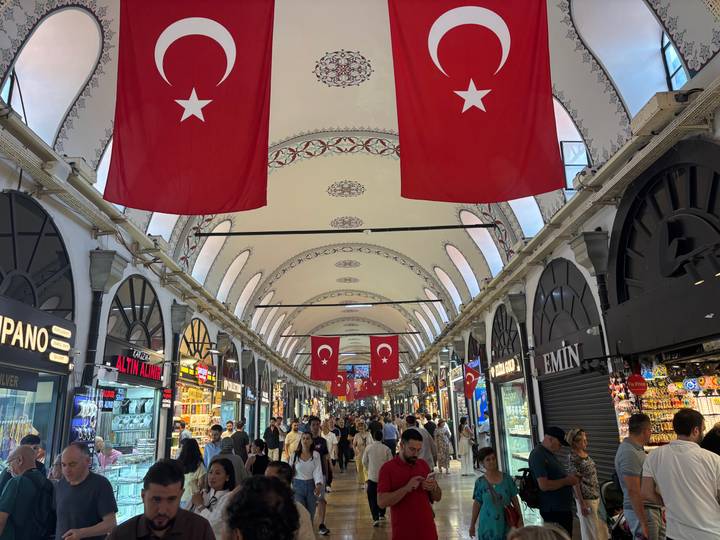 Shoppers wander beneath arched ceilings lined with Turkish flags and glittering shops in the Grand Bazaar.