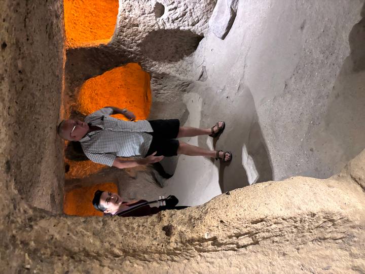 Tourists explore a dimly lit chamber of Cappadocia’s underground city, its walls glowing orange from lights.