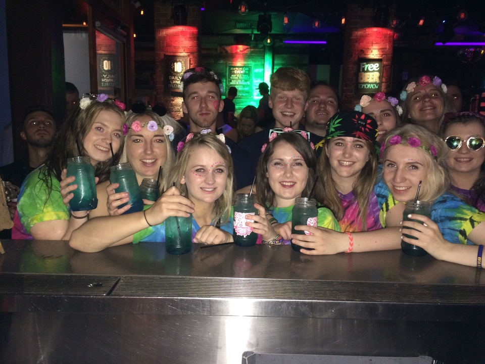 Group of friends enjoying drinks with colorful lights in the background.