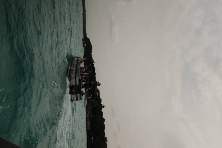 Motorboat carrying passengers speeds across turquoise water under a hazy sky.
