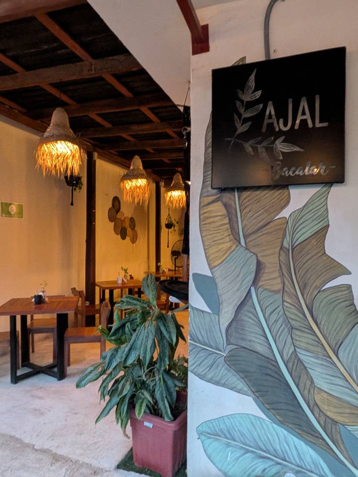 Cozy café interior with wooden tables, woven lamps and leafy wall mural.