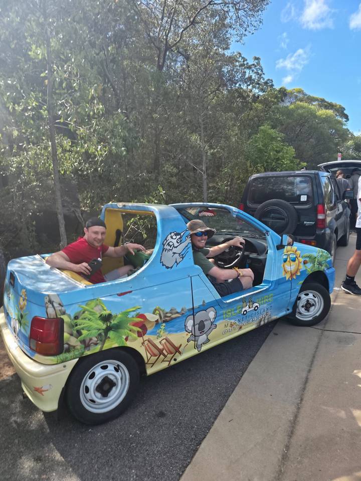 Two travellers sit in colourful open-top mini car decorated with island art
