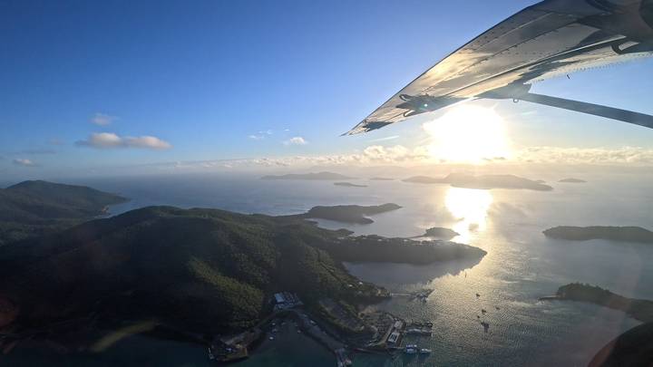 Aerial view of island-studded sea from plane wing with bright sun reflection