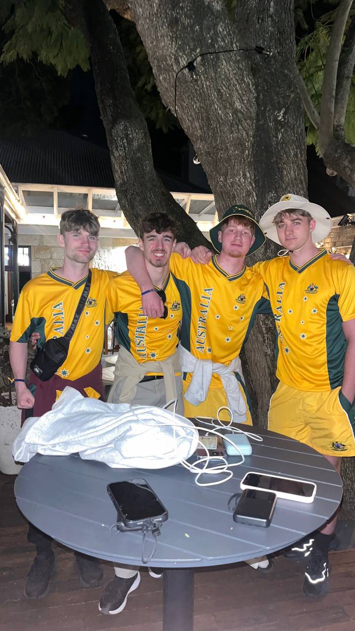 Group of four young men wearing matching yellow Australia jerseys posing indoors with arms around each other