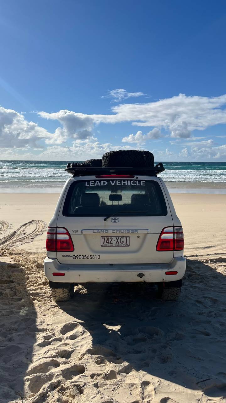 Toyota Land Cruiser marked 'Lead Vehicle' parked on a wide sandy beach facing rolling surf