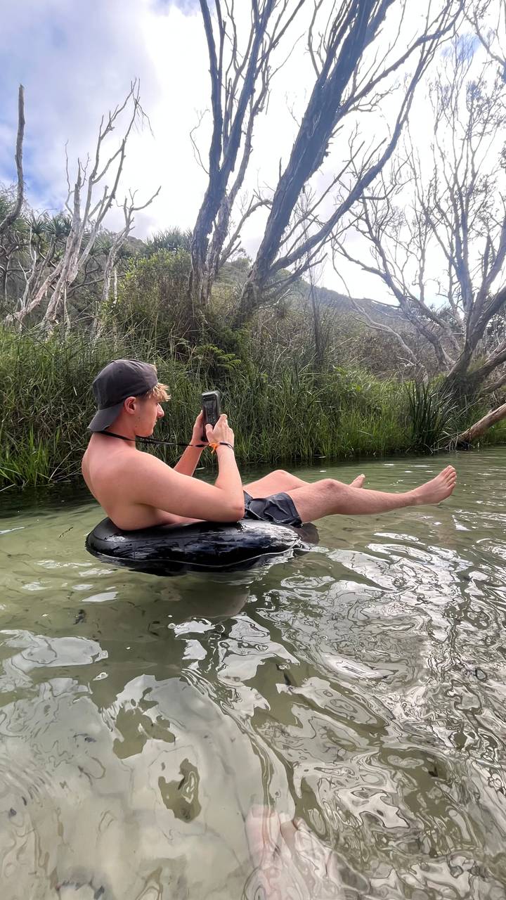 Man reclines on an inner tube in a calm freshwater creek surrounded by dense vegetation