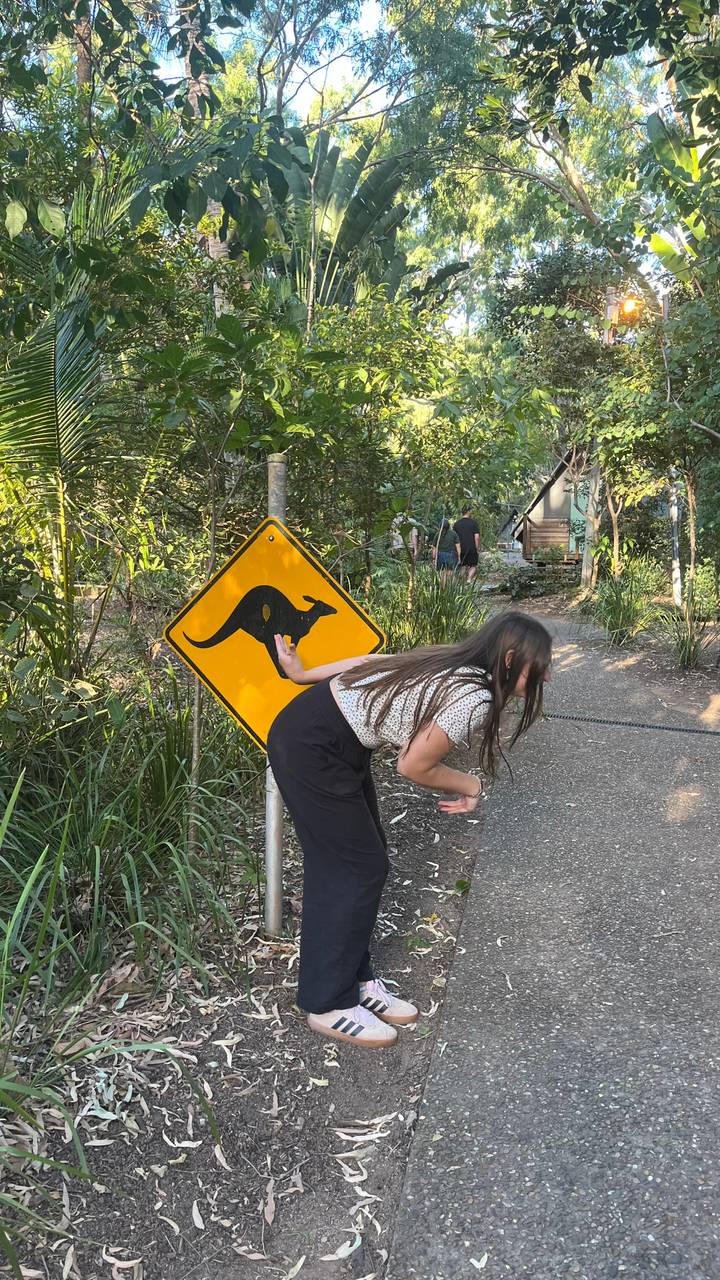 Woman playfully posing beside a yellow kangaroo crossing sign on a forest path