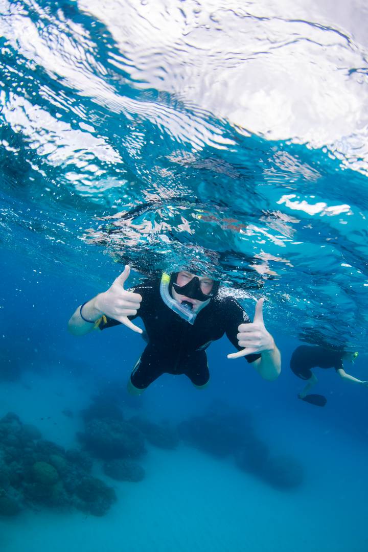 Underwater shot of a snorkeller giving shaka hand signs beneath clear blue water