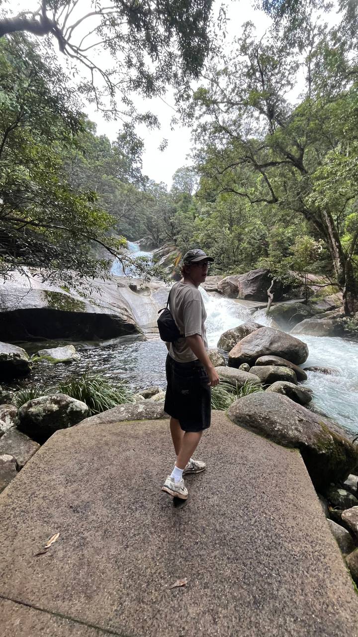 Traveller standing on rocks beside a rushing rainforest stream and small cascade