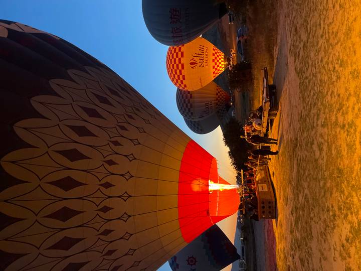 Ground crew prepare a hot-air balloon as bright flames illuminate the envelope before takeoff at dawn.