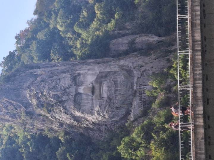 Towering rock carving of Decebalus’s face overlooks the Danube gorge as tourists cross a bridge below.