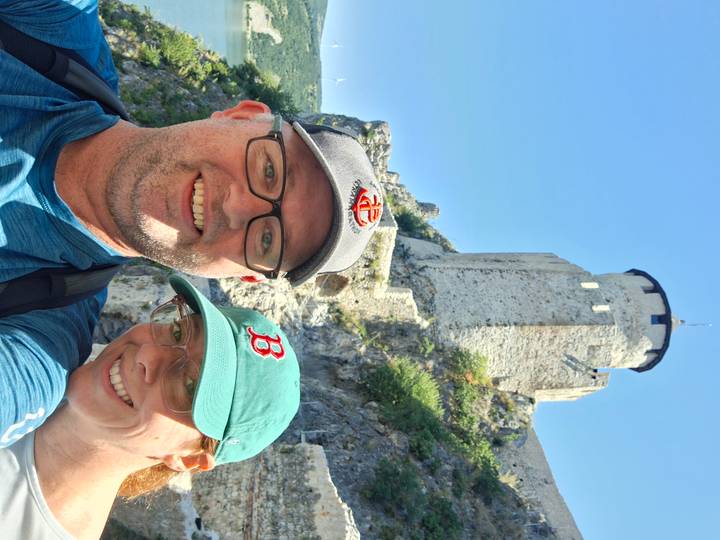 Smiling couple selfie with the medieval towers of Golubac Fortress rising behind them under clear skies.