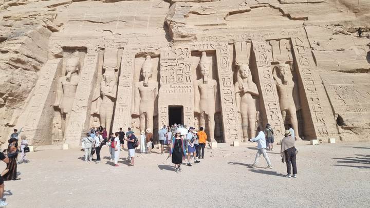 Crowds gather in front of the colossal statues and hieroglyphs carved into the facade of Abu Simbel Temple.