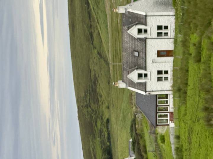 White stone cottage set amid rolling green moorland under a cloudy sky.
