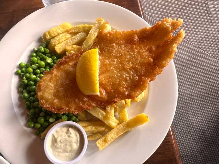 Plate of golden battered fish with chips, peas and tartar sauce.