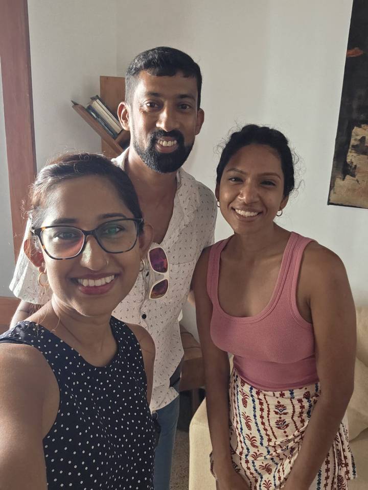 Indoor close-up selfie of three smiling travellers standing together in casual clothing.