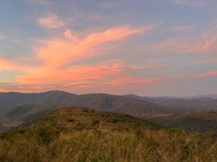 Vivid pink clouds over rolling green hills at sunset.
