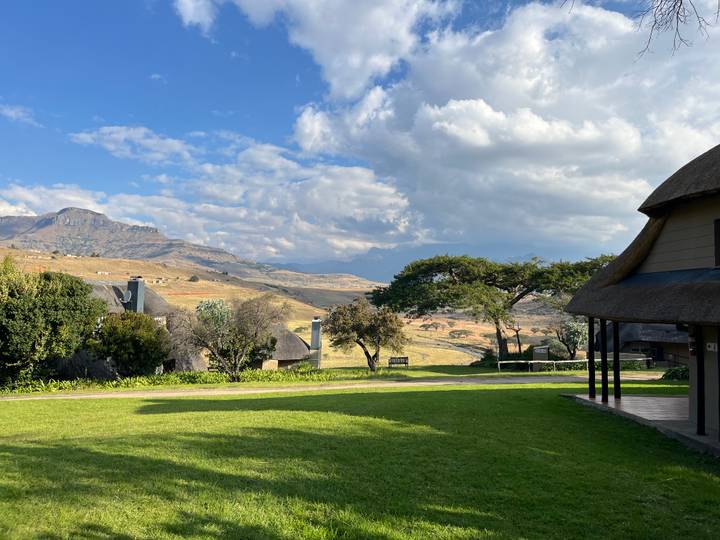 Mountain resort lawn with thatched cottages, dramatic peaks and patchy clouds.