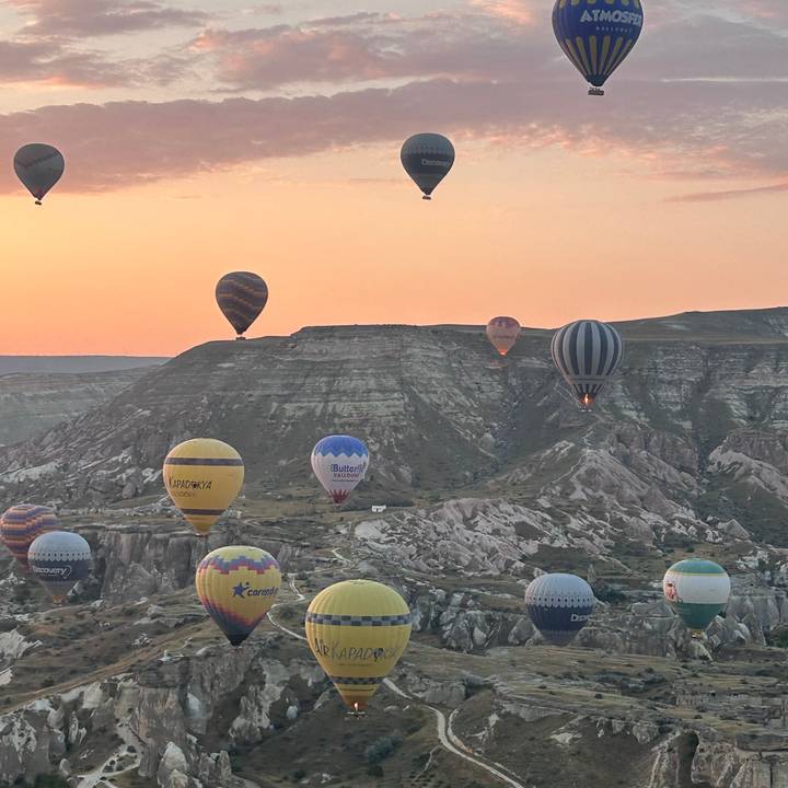 Hot-air balloons float in front of striped mesas at dawn, one basket illuminated by burner flame.