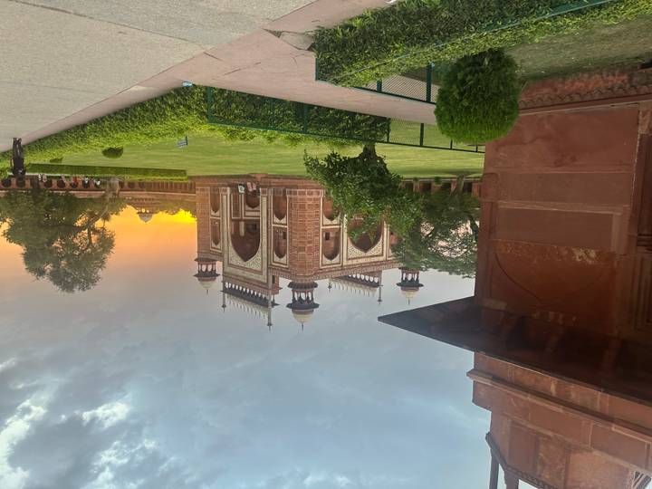 Sunset illuminates the red sandstone gateway to the Taj Mahal complex set amid manicured lawns.