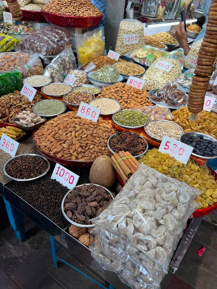 Colorful display of nuts, spices and dried fruits with price tags at an outdoor market stall.