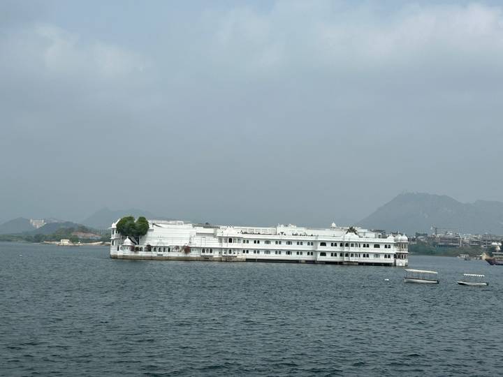 Lake Palace hotel floating on a calm lake with hazy mountains and city in the background.