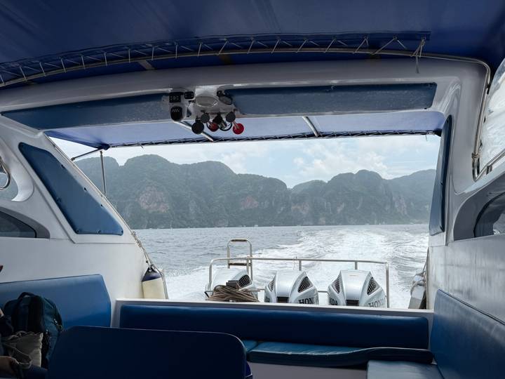 View from the back of a speedboat leaving a foamy wake toward towering green limestone cliffs.