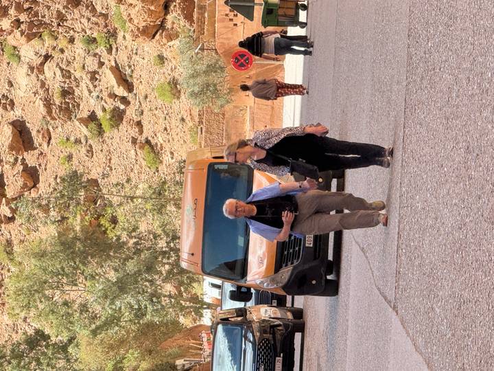 Tourists walking near parked vans against rocky mountain backdrop in Morocco.