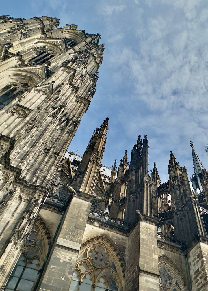 Soaring Gothic spires and ornate stonework of a cathedral captured from a dramatic low angle against a blue sky.