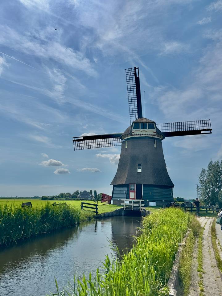 Traditional Dutch windmill standing over flat green fields beneath a blue sky with scattered clouds.