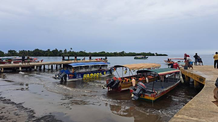 Small motorboats tied to a wooden pier with passengers boarding beside a calm bay.