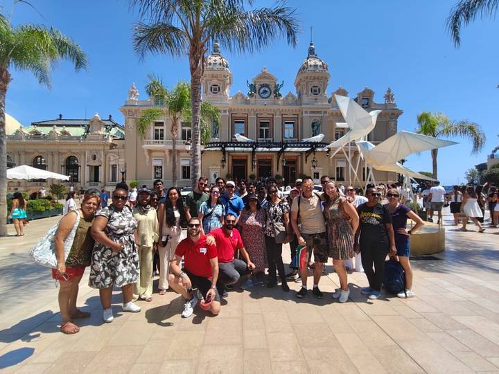 Cheerful tour group gathered outside the ornate Monte Carlo Casino under bright blue sky