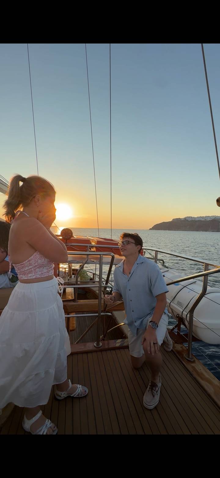 Man kneeling with engagement ring proposing to surprised partner on a sailboat at sunset