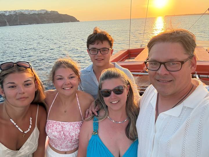 Family selfie on boat deck with calm sea and setting sun in background