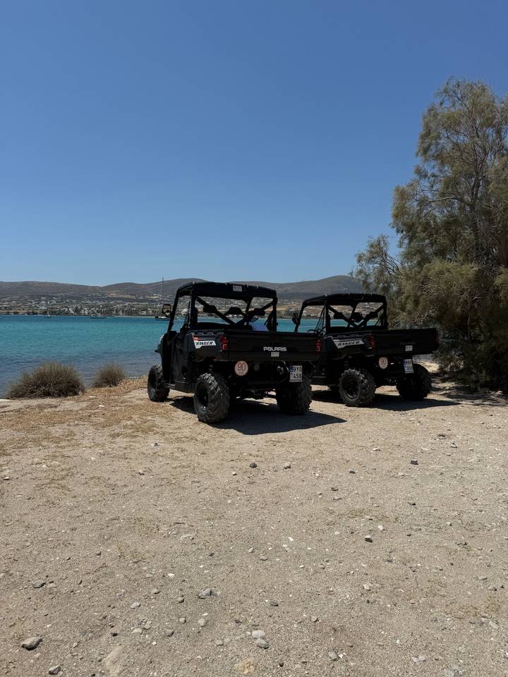 Two off-road Polaris utility vehicles parked beside turquoise bay under clear sky