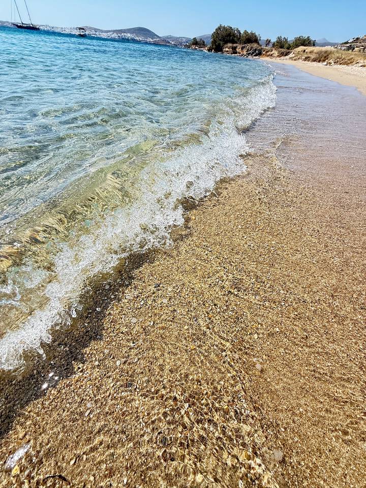 Close-up of small wave washing over golden pebbly beach creating frothy pattern
