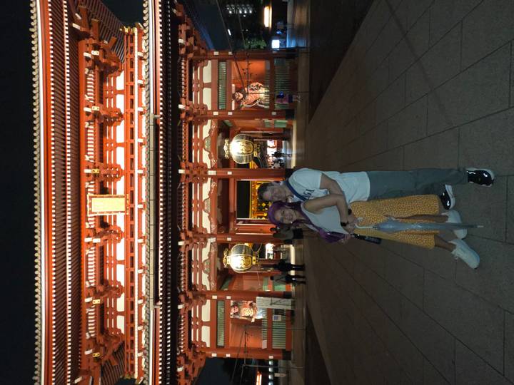 Couple pose in front of the brightly lit gate of Senso-ji temple at night.