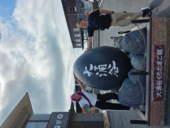 Travelers stretch arms around the famous giant black egg monument in volcanic Owakudani.