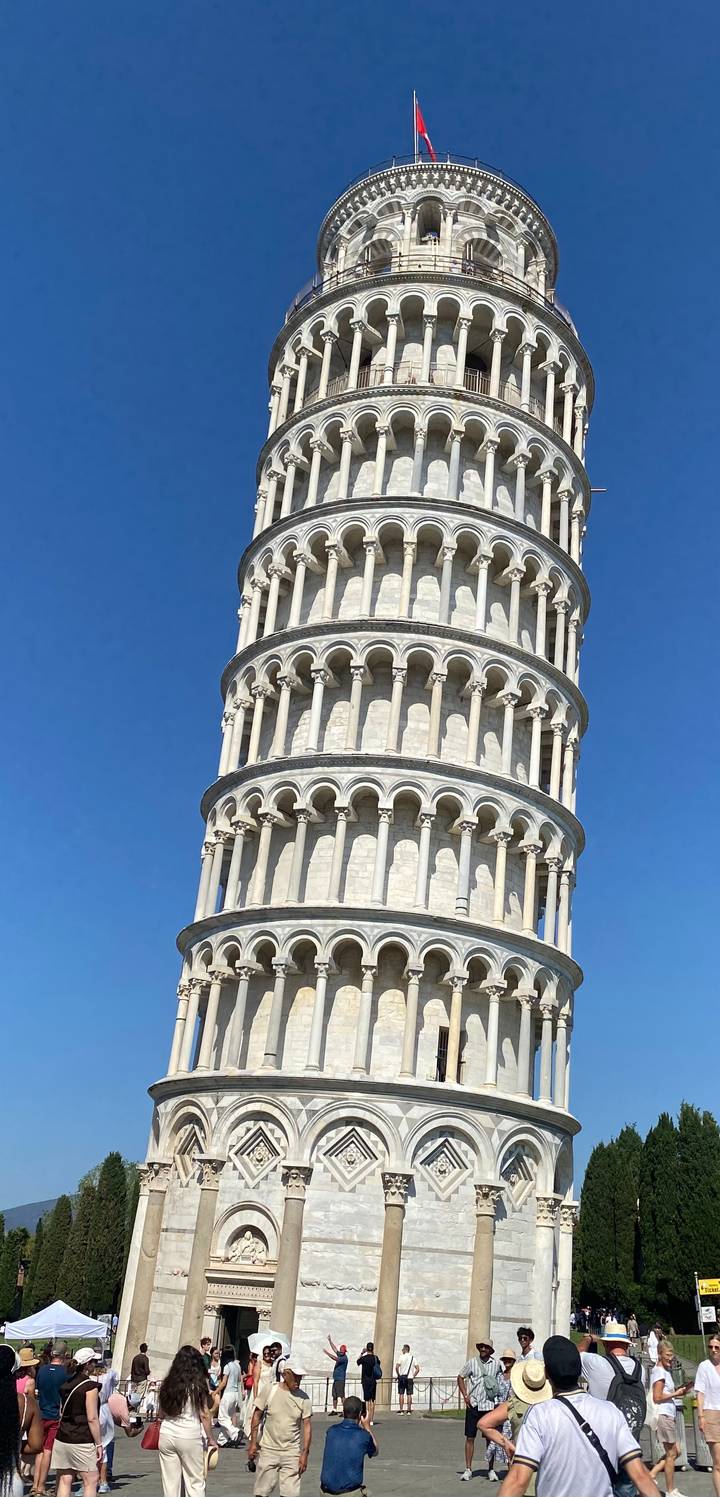 Detailed upward view of the Leaning Tower of Pisa showcasing its iconic Romanesque arcades against a clear blue sky.