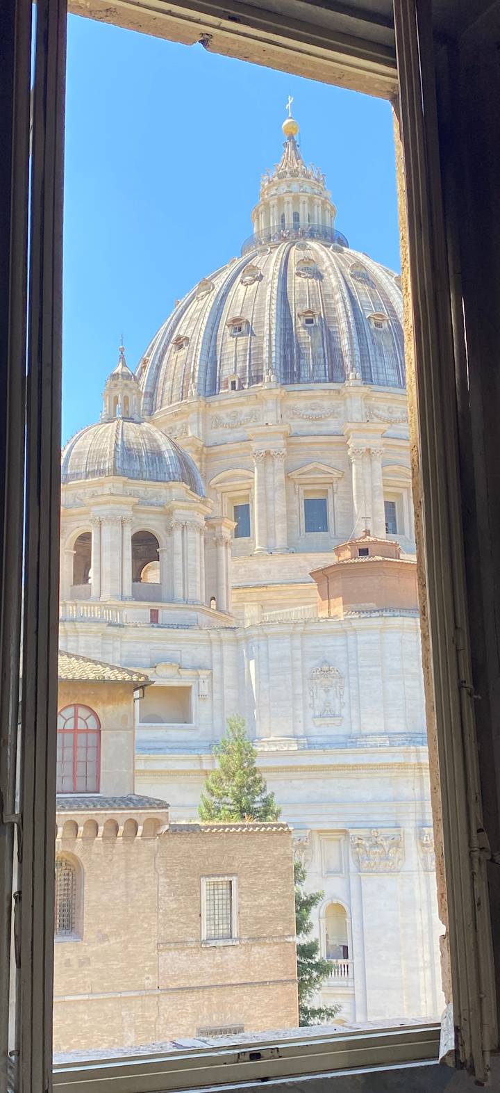 Architectural dome and colonnades of a grand basilica seen through an open window frame.