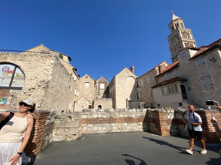 Visitors explore stone walls and Romanesque buildings within Diocletian’s Palace under a clear Croatian sky.