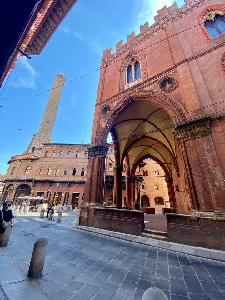 Arched portico and medieval Asinelli Tower rise above Bologna’s historic red-brick square.
