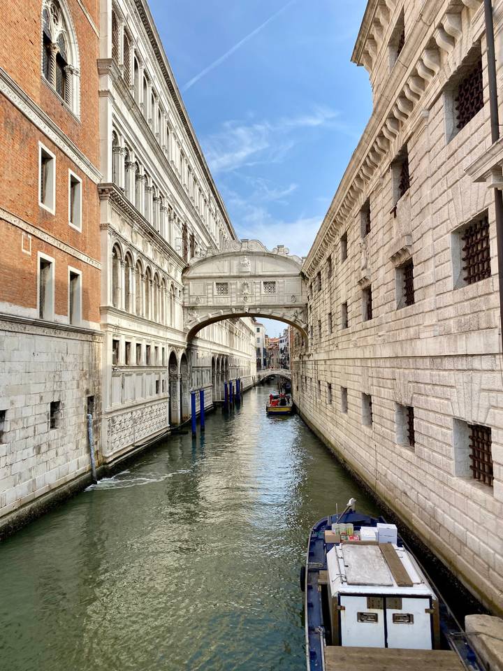 Elegant white limestone Bridge of Sighs arches over a narrow Venetian canal with a gondola passing beneath.
