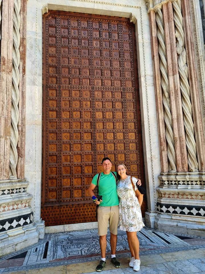 Couple posing in front of a grand carved wooden cathedral door framed by marble columns