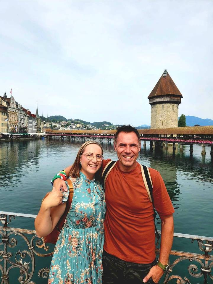 Couple smiling with Lucerne’s Chapel Bridge and water tower reflected in the Reuss River behind them