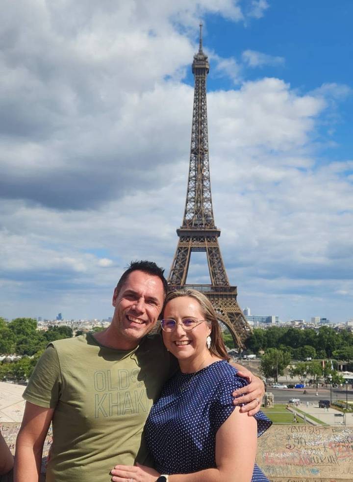 Couple posing with the Eiffel Tower rising behind them under partly cloudy skies