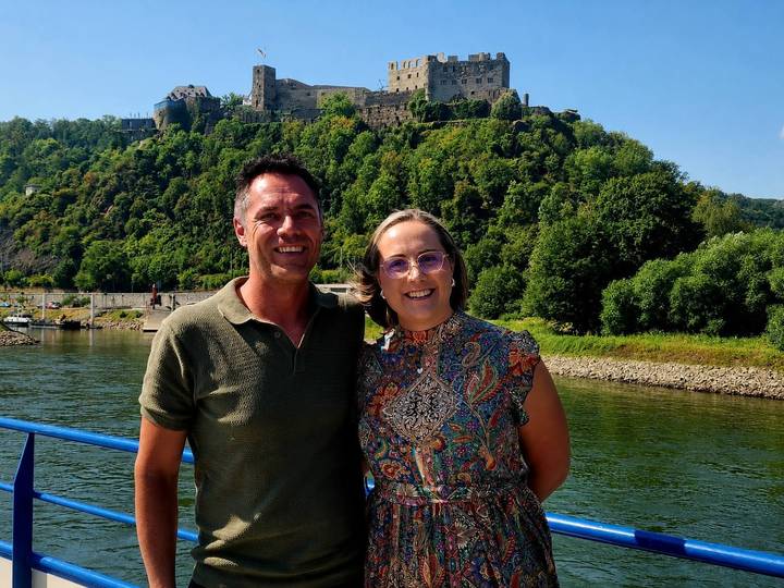 Couple on a river boat with a hill-top Rhine castle and green forested slopes behind