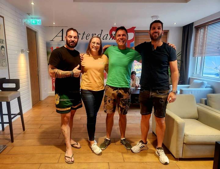 Four travellers posing happily inside a hostel lounge with an Amsterdam poster behind