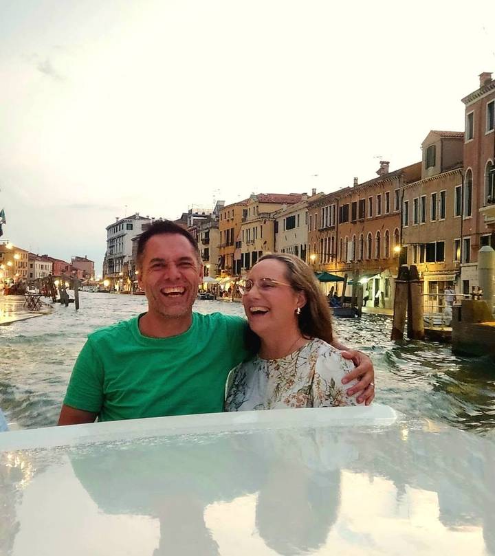 Laughing couple on a boat ride along Venice’s Grand Canal at dusk with lit buildings