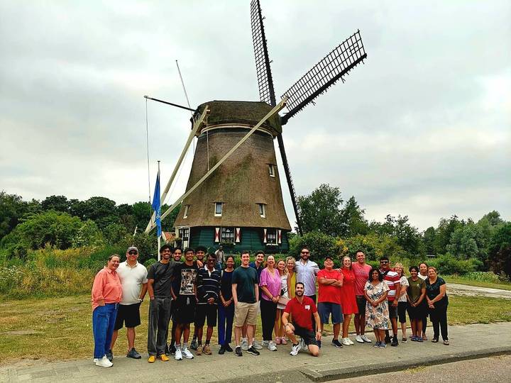 Large tour group posing in front of a traditional Dutch windmill set in green countryside